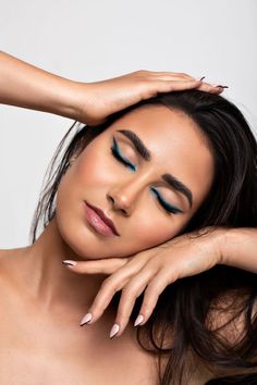 a woman with blue eyeshadow and long nails posing in front of a white background