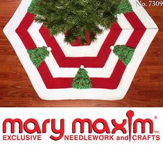 a red and white knitted christmas tree skirt with pine trees on it, sitting on a wooden floor