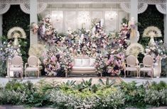 a stage set up with chairs and flowers on the wall, surrounded by greenery