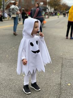 a little boy dressed up as a ghost with a toothbrush in his mouth while standing on the street