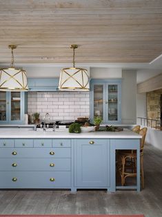 a kitchen with blue cabinets and gold pulls on the doors, two hanging lights over the island