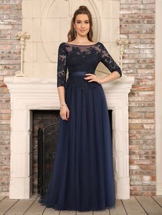 a woman standing in front of a fireplace wearing a long blue dress with sheer sleeves