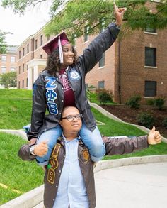 a man is carrying a woman on his shoulders in front of a brick building and trees