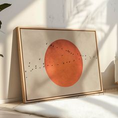 an orange circle with birds flying in front of it on a white wall next to a potted plant