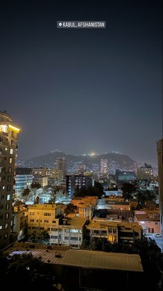 the city is lit up at night with bright lights in the buildings and mountains behind it