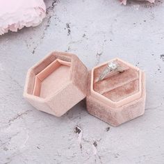 an open ring box sitting on top of a cement floor next to pink flower petals