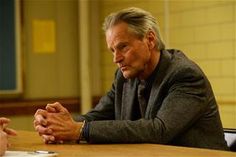 an older man sitting at a table with his hands folded and looking off to the side