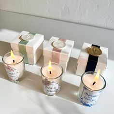 three candles are sitting in front of small boxes with labels on them and one candle is lit