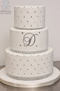 a three tiered white wedding cake with diamonds on the bottom and monogramming