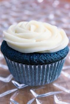 a blue cupcake with white frosting sitting on top of a glass tablecloth