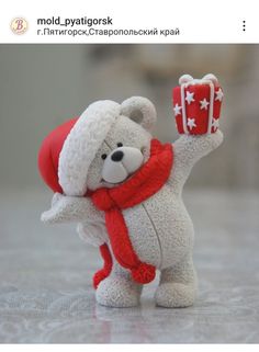 a white teddy bear with a red scarf and hat holding a gift box in his hand