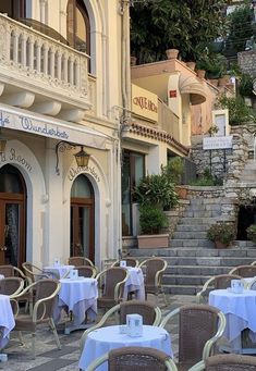 an outdoor dining area with tables and chairs on the side of the street in front of a building