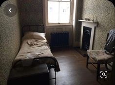 a small room with a bed, chair and fireplace next to a window in the corner