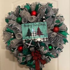 a christmas wreath on the front door decorated with green, red and silver ribbon bows