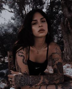 a woman with tattoos sitting on a bench next to a tree and snow covered ground