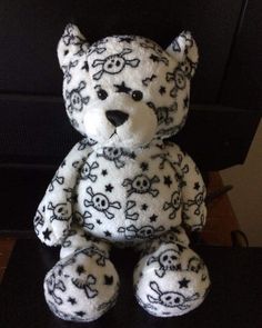 a white teddy bear with black skulls and stars on it's chest sitting in front of a television