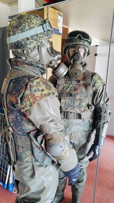 two soldiers in gas masks and protective gear standing next to each other with their hands on their hipss