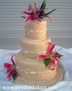 a three tiered wedding cake with pink flowers on the top and bottom, sitting on a white table cloth