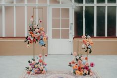 two tall floral arrangements sitting on top of a rug in front of a building with windows