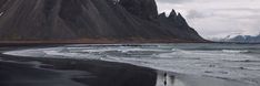 two people walking on the beach in front of mountains