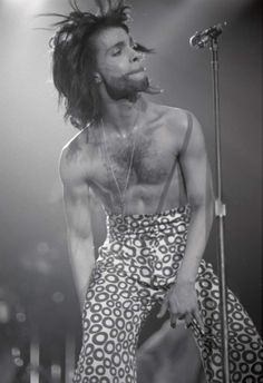 a man with long hair standing in front of a microphone and wearing an animal print pants