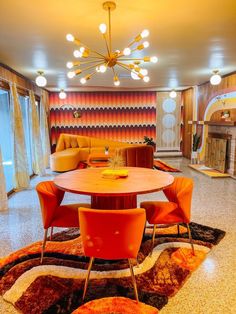 a living room filled with furniture and a round table surrounded by orange chairs in front of a fire place