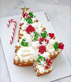 a decorated gingerbread christmas tree on top of a piece of paper next to a candy cane