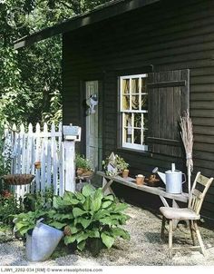 a black house with a white picket fence and potted plants on the front porch