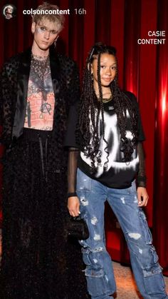 two people standing next to each other in front of a red curtain