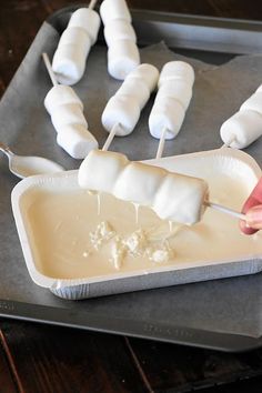 someone is dipping marshmallows into melted cheese on a baking sheet with toothpicks