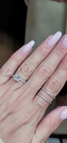 a woman's hand with pink manies and two rings on her fingers, holding an engagement ring