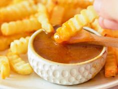 a person dipping sauce into french fries on a plate