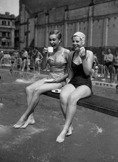 two women in bathing suits sitting on a bench drinking tea and talking to each other