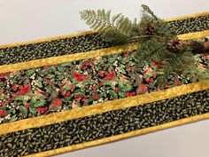 a table runner with pine cones and red berries on it, along with evergreen needles