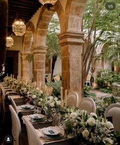 a long table with white flowers and greenery is set for an elegant dinner party