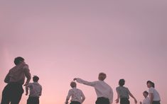 a group of people standing on top of a beach next to the ocean under a pink sky