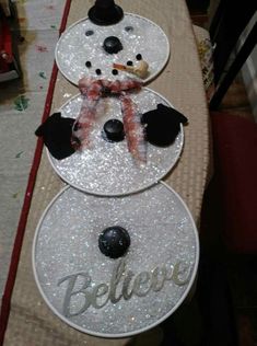 three snowmen sitting on top of a table covered in glitter and plastic plates with the word believe written on them