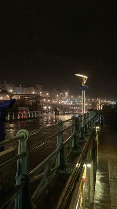 people are walking on the boardwalk at night with umbrellas and lights in the rain