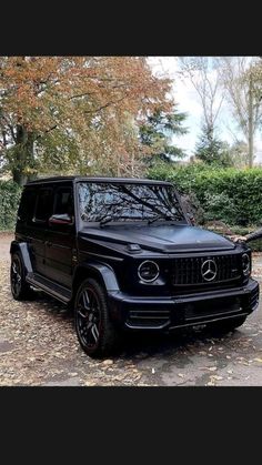 a man standing next to a black mercedes g - class parked in front of trees