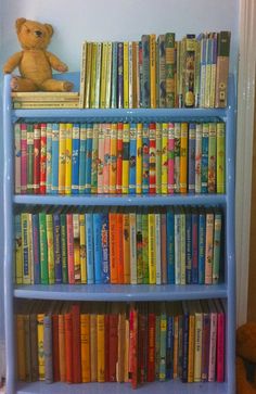 a blue book shelf filled with books next to a teddy bear on top of it