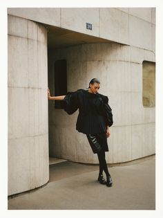 a woman in black is leaning against a wall