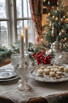 a christmas table setting with candles, cookies and other holiday treats on it in front of a window