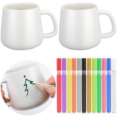 two white coffee mugs with colored markers on them and one is holding a pen