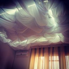 an air conditioner sitting next to a window covered in white sheer curtains and drapes