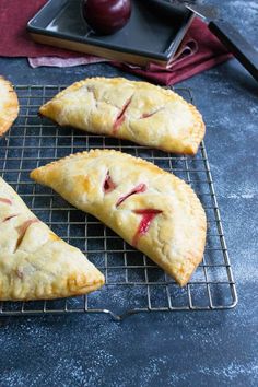 four pieces of pie sitting on top of a cooling rack next to an apple and knife