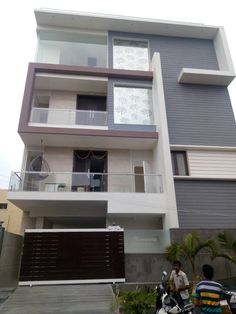 two men riding mopeds in front of a modern house with balconies