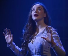 a woman standing in front of a blue background holding her hands out to the side