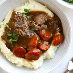 a white plate topped with mashed potatoes covered in meat and gravy next to green beans