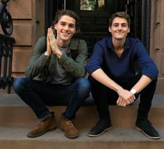 two young men sitting on steps in front of a door with their hands together and smiling