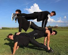 three men in black shirts and pants are on the grass with one man upside down